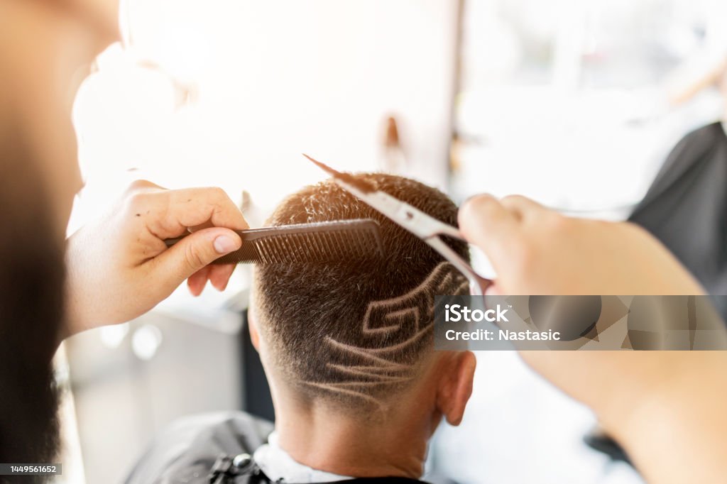 Barber shaving designs into a clients hair holding scissors Hairdresser working in barber shop Hair Salon Stock Photo