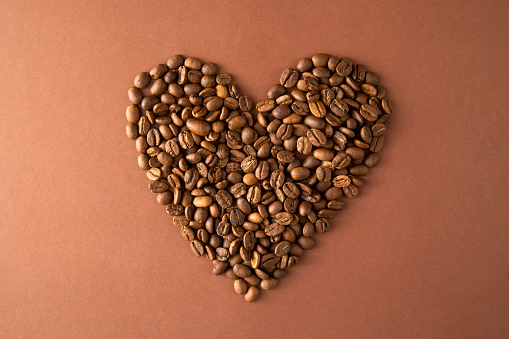 Heart coffee. Roasted coffee beans in the shape of heart on bright stone background. Concept of coffee love, Valentines Day, good mood, gift. With wooden spoon.
