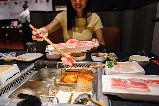 Asian woman enjoying traditional Chinese hotpot with assorted fresh and scrumptious ingredients in restaurant.