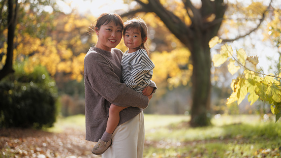 A mother and her small daughter are spending time together in a park in autumn.