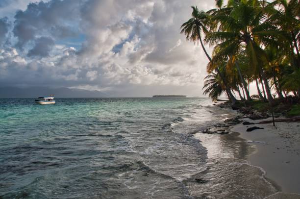 un pequeño bote cerca de la costa de una isla tropical durante la puesta de sol - panama caribbean culture san blas islands caribbean fotografías e imágenes de stock