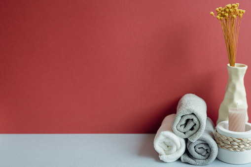 Stack of rolled shower cotton towels and candle, vase of dry flower. bathroom spa concept. red and gray background