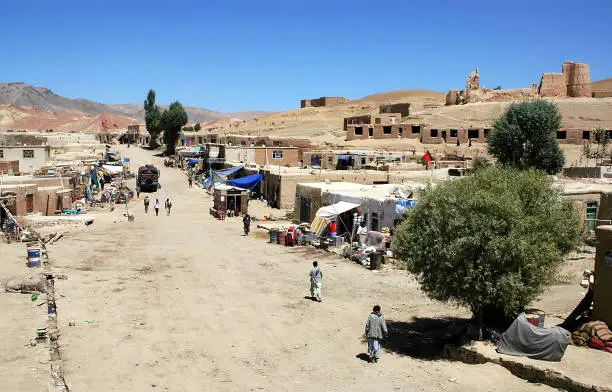 Lal Wa Sarjangal, Ghor Province in Central Afghanistan. This is the dusty main street in Lal. The low basic buildings and dirt road are typical in remote towns in Afghanistan. Note the Afghan flag. (Unrecognizable people)