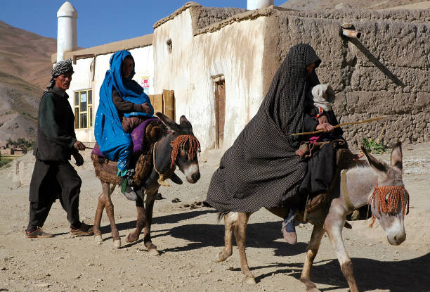 An Afghan man walks behind two women riding donkeys in the town of Syadara in Central Afghanistan stock photo