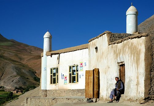 Syadara (Siyah Darah), Bamyan (Bamiyan) Province / Afghanistan: An Afghan man sits outside a mosque in the small town of Syadara in Central Afghanistan. Man with skull cap outside mosque