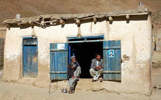 Syadara (Siyah Darah), Bamyan (Bamiyan) Province / Afghanistan: Two Afghan men sit in a house doorway in the small town of Syadara in Central Afghanistan. Man with turban and tea kettles