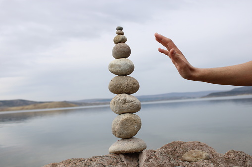 A hand constructs equilibrium on pebbles. Perfect balance of stack of pebbles on the seashore. Concept of balance, harmony and meditation. Helping or supporting someone for growing or going higher.
