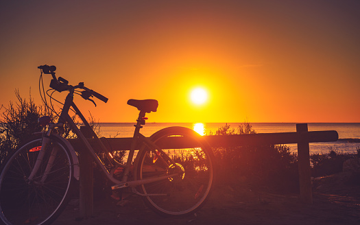 Bicycle outdoor parked on beach, evening time, sunset sky. Holidays, sport and recreation.