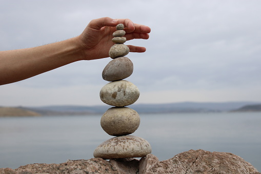 A hand constructs equilibrium on pebbles. Perfect balance of stack of pebbles on the seashore. Concept of balance, harmony and meditation. Helping or supporting someone for growing or going higher.