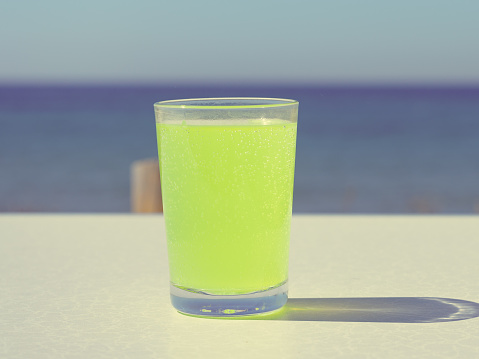 Flavored citrus drink in glass on table, sea water in the background