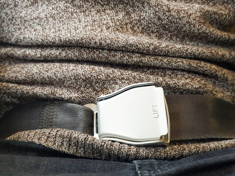 Close-up of a man wearing a secured safety belt on an airline journey.