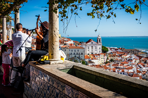 Lisbon, Portugal - November 01, 2022: aerial view over the rooftops of Lisbon. Woman playing guitar and singing. Tagus River in background.