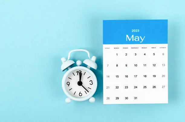 Photo of The May 2023 Monthly calendar for 2023 year with vintage alarm clock on blue background.