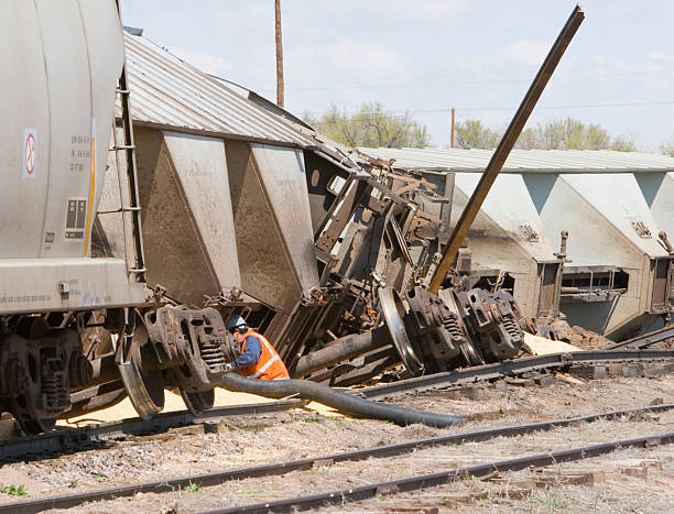 Several railroad cars of corn are derailed. The worker is vacuuming corn from one of the cars.