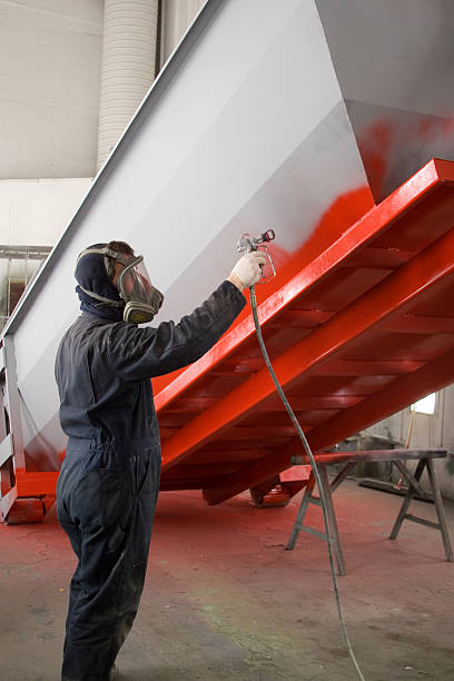 Painter in a respirator mask spray painting container orange stock photo