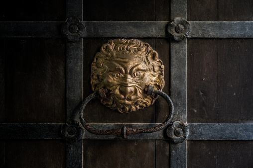 Rustic door knocker in the shape of a lion head, painted gold, on an old medieval wooden door