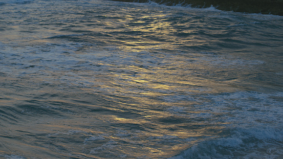 Beautiful dark sea at dusk. Golden setting sun reflecting on the roaring waves