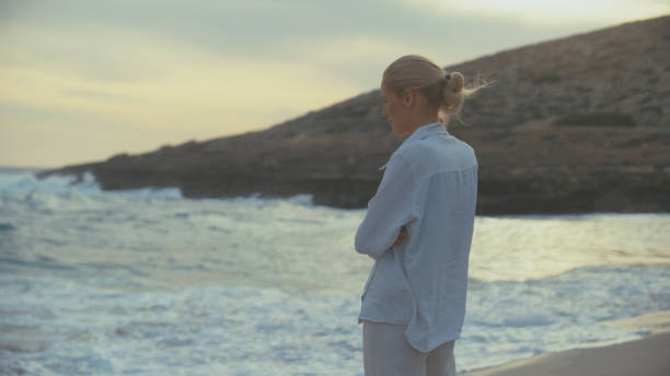 istock Woman standing alone on a beach. Looking off into distant sea 1449598648