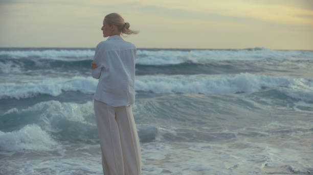 istock Woman standing alone on a beach. Looking off into distant sea enjoying the light breeze 1449599329