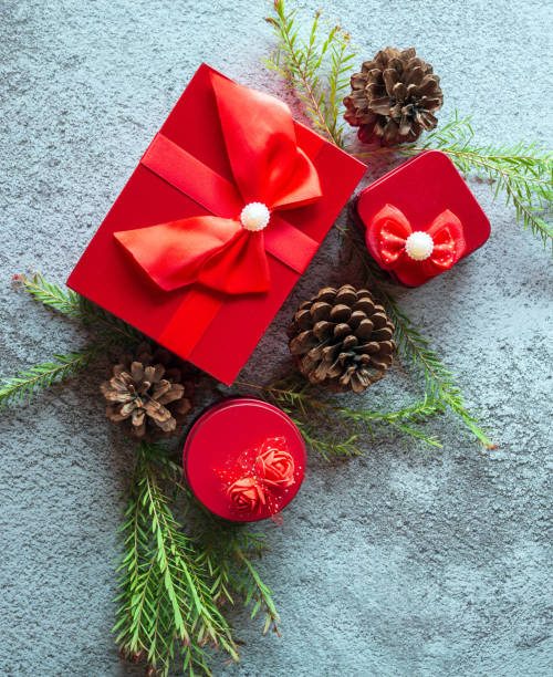 composition de décoration de noël sur fond de béton gris avec un beau coffret cadeau rouge avec ruban rouge, branches d’arbres et pommes de pin - pine nut tree pine tree pine cone photos et images de collection