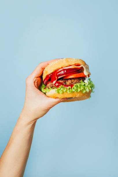 파란색 배경에 여성 손에 햄버거를 클로즈업 - take out food burger bun hamburger 뉴스 사진 이미지