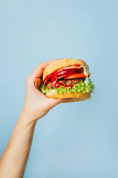 Photo of close-up on a hamburger in a female hand on a blue background