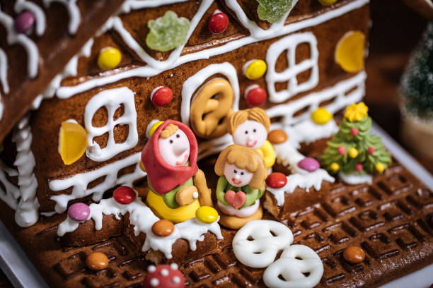 Christmas house made from gingerbread. Playfully decorated with colourful gummy bears. Christmas tree in background with lights. Festive New year atmosphere and mood.