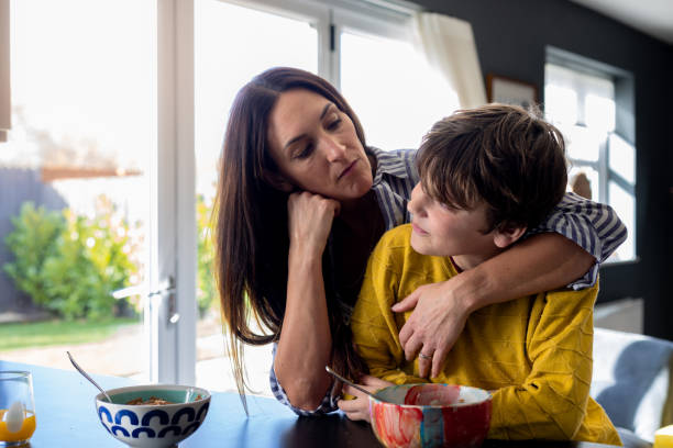A Disappointed Mother Looking at Son A waist-up shot of a mother reaching her arm around her son next to the kitchen counter looking unhappy with her son. They are wearing casual clothing. worried mom with kids stock pictures, royalty-free photos & images