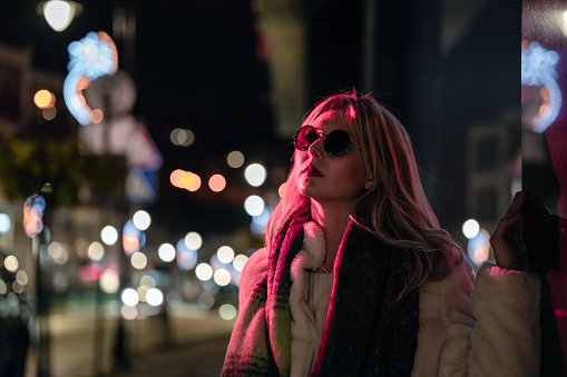 Portrait of woman with sunglasses standing on the streets lit with red neon lights
