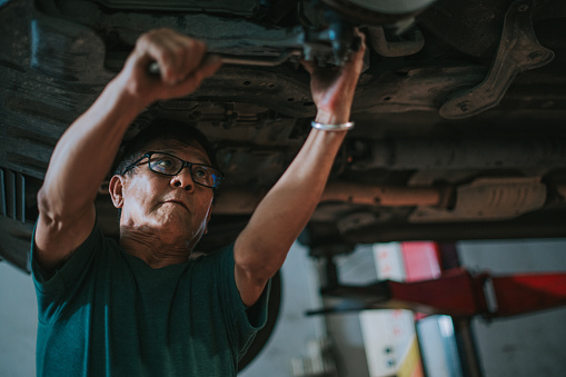 Asian Chinese senior mechanic checking car undercarriage in auto repair shop