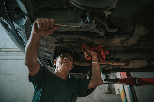 Asian Chinese senior mechanic checking car undercarriage in auto repair shop