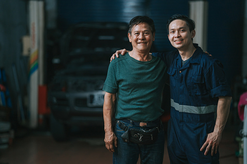 portrait 2 Asian Chinese mechanic looking at camera smiling standing in front of auto repair shop