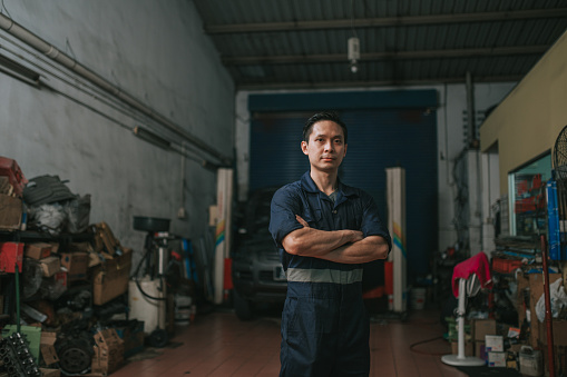 portrait Asian Chinese mechanic looking at camera standing in front of auto repair shop