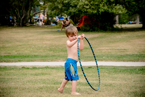 The three year old boy is learning how to use the hulahoop, he isnt very good at it yet.