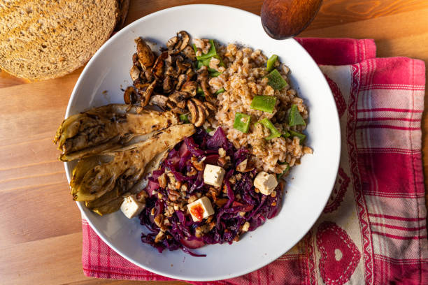 view of winter vegetarian bowl with red cabbage, mushrooms, tofu, spelt cereal, endive and radicchio on wooden table. Example of winter or autumn season homemade vegan dish stock photo