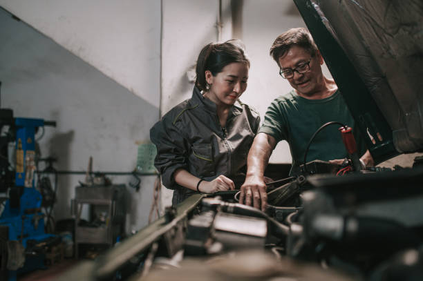 senior asian chinese mechanic guiding trainee checking battery level in auto repair workshop - trainee working car mechanic imagens e fotografias de stock