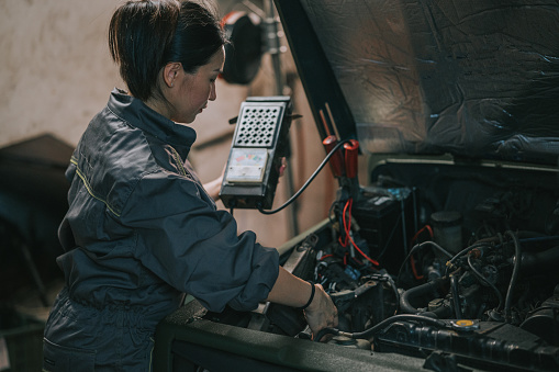 Asian Chinese female Mechanic checking battery level in auto repair workshop
