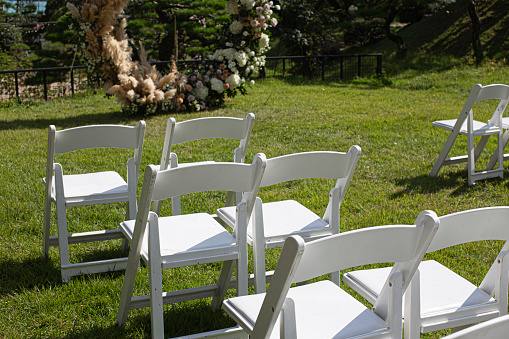 Rows of empty white folding chairs sitting on a lawn.