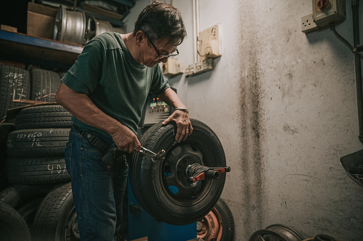 Asian Chinese senior male mechanic worker balancing wheel alignment tyre repairing it with machine in Auto repair shop