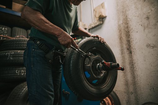 Asian Chinese senior male mechanic worker balancing wheel alignment tyre repairing it with machine in Auto repair shop