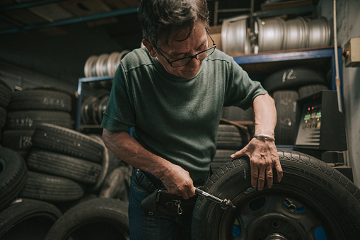 Asian Chinese senior male mechanic worker balancing tyre adjusting it with machine in Auto repair shop