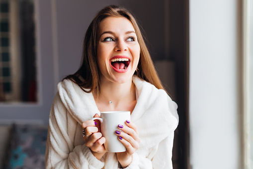 A girl with an emotional smile holding a cup of tea or coffee.  Awake morning.