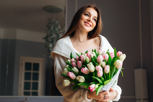 Good morning! Attractive young woman with bouquet of white and pink tulips is spending time at home.