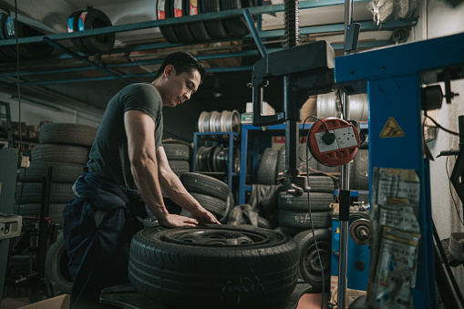 Asian Chinese male mechanic worker changing tyre extracting it with machine in Auto repair shop