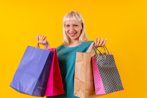 smiling shopping with bags on sale, blonde caucasian girl in studio on yellow background