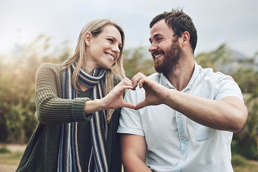 Couple, hands and smile with love gesture for happy relationship bonding and care in the outdoors. Hand of man and woman smiling together in happiness with heart shape sign for romance in nature park