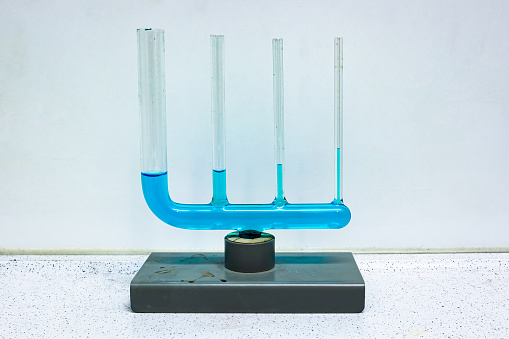 Glass equipment where several different connected tubes are filled with a blue liquid, demonstrating capillary action. Used in physics class.