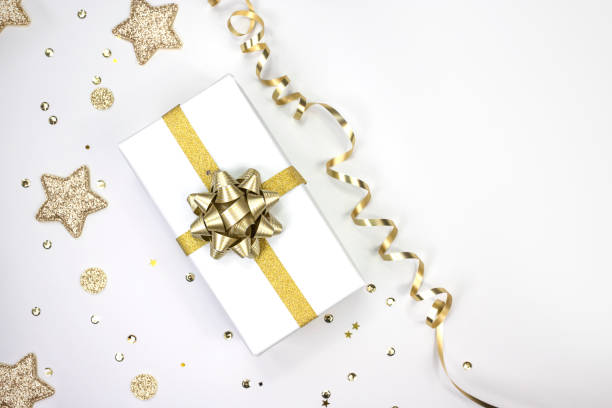 istock Christmas present in white paper with gold bow on white background studded with sequins. Top view, space for text. 1449629053