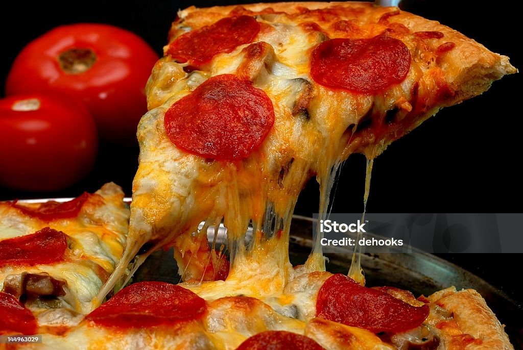 Pepperoni Pizza Slice Slice of pepperoni pizza being removed from whole pizza with tomatoes in background.  Isolated on black background. Black Background Stock Photo