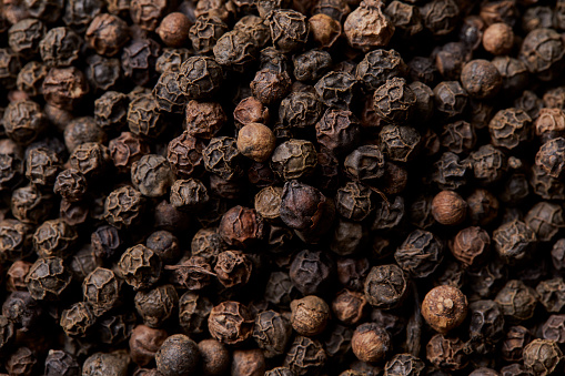 Dry black pepper seasoning, in a handmade wooden bowl on an oak wooden table top, a top view macro photo shoot texture background, image with a large copy space